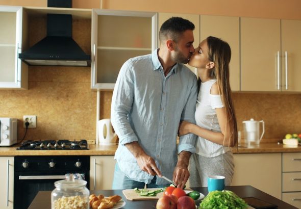 Happy young couple in the kitchen. Handsome man meet and kiss his girlfriend early morning at home