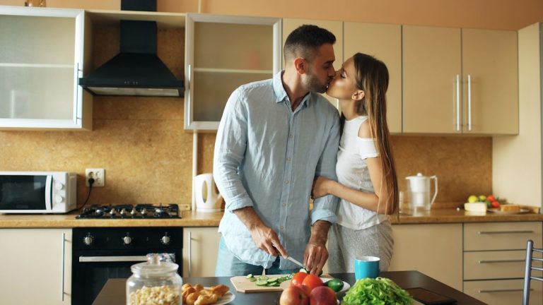 Happy young couple in the kitchen. Handsome man meet and kiss his girlfriend early morning at home