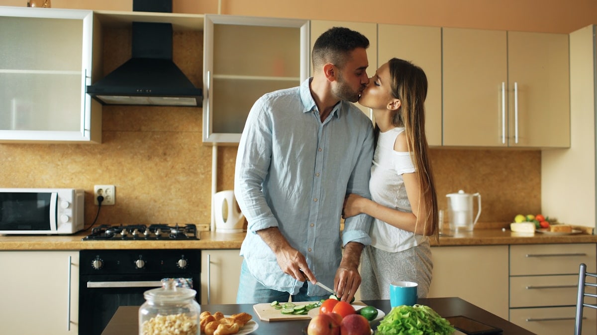 Happy young couple in the kitchen. Handsome man meet and kiss his girlfriend early morning at home